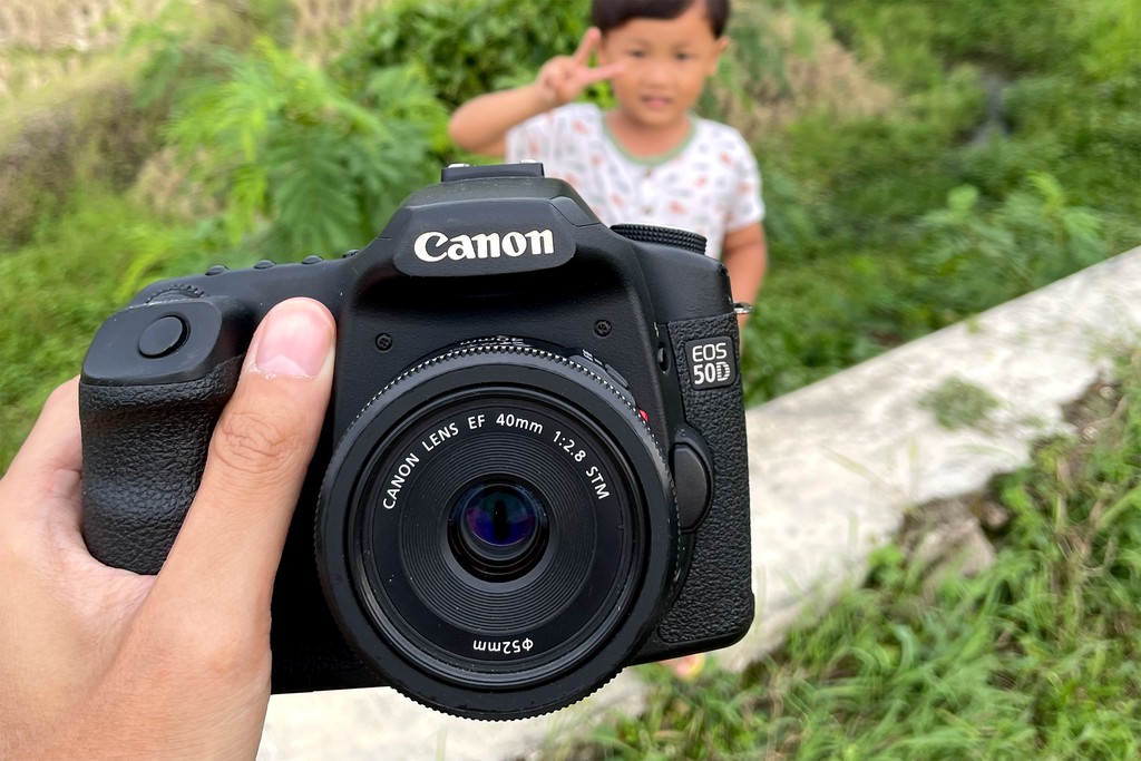 Tangan memegang kamera Canon EOS 50D dengan lensa EF 40mm f/2.8 STM